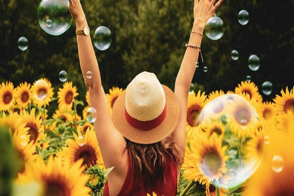 woman with arms up in sunflower field with bubbles