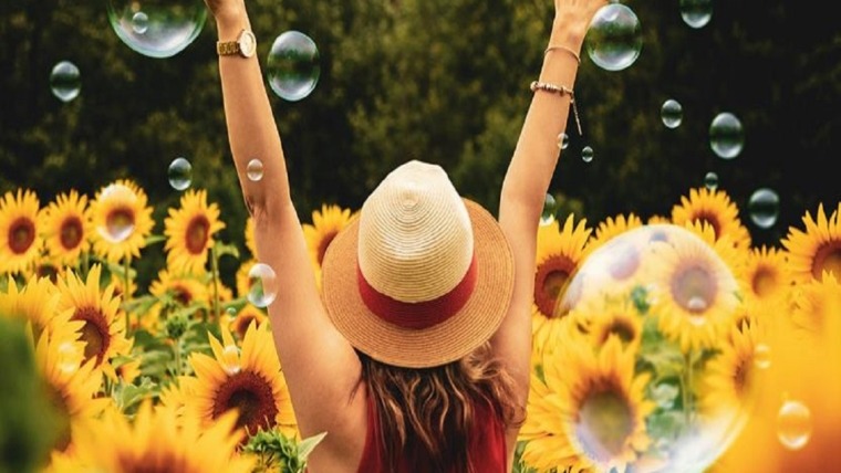 woman with arms up in sunflower field with bubbles