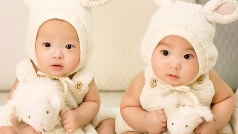 2 asian babies dressed in light onsies with rabbit ears