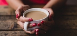 womans hands with ren nail polish holding white cup of coffee