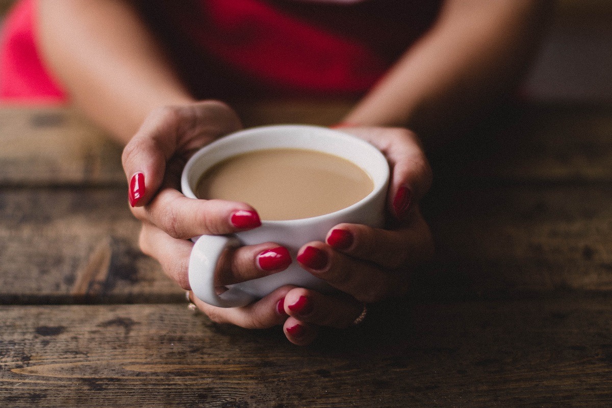 womans hands with ren nail polish holding white cup of coffee