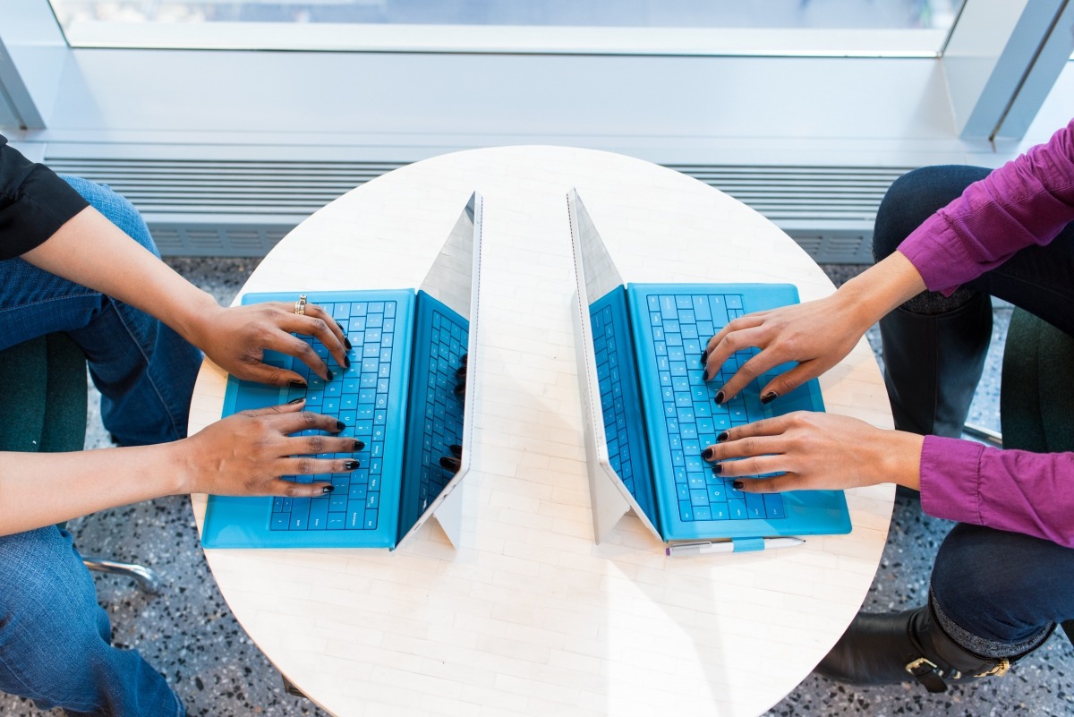 2 blue laptops with hands typing on each