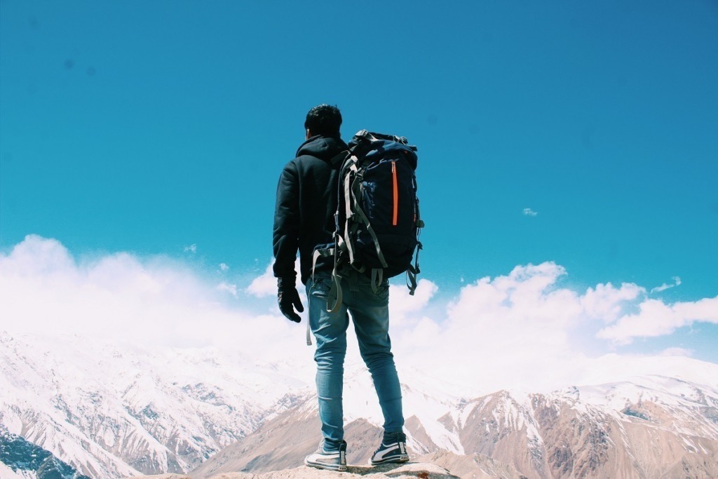 man with backpack looking at snow topped mountains