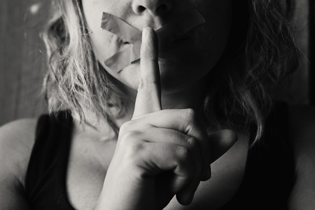 woman with mouth taped and finger to face