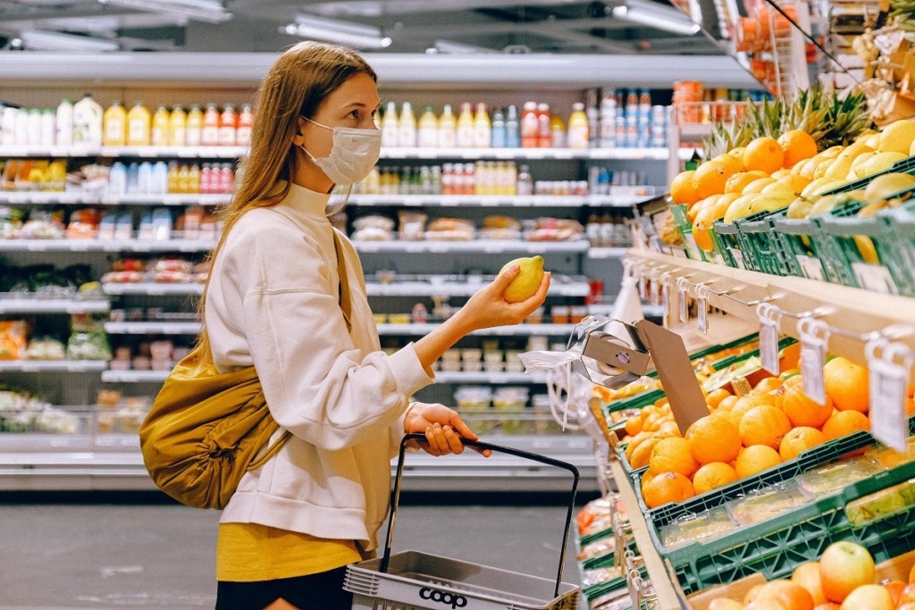 woman with mask holding lemon at grocer