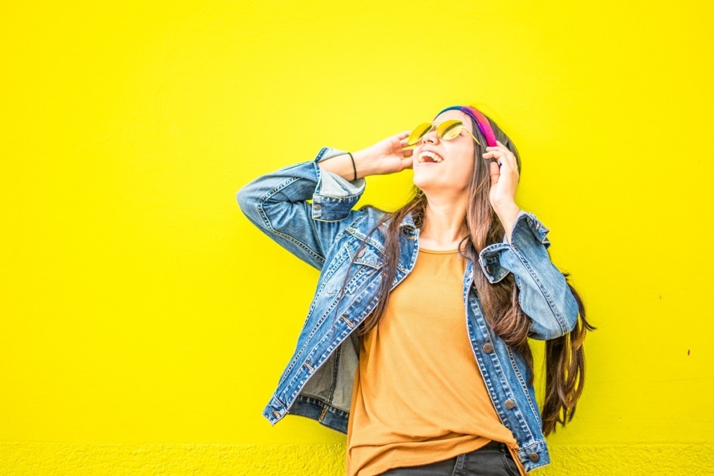 girl with headband and glasses laughing against a yellow backdrop