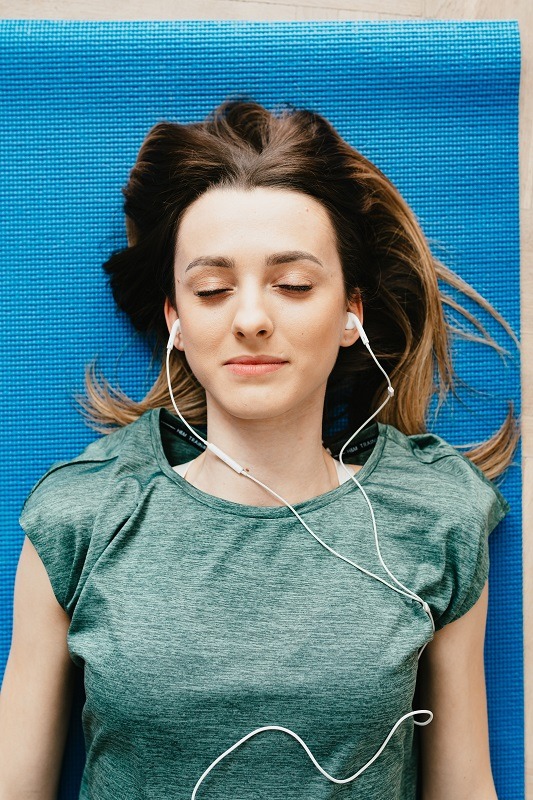 woman lying on blue yoga mat with earphones