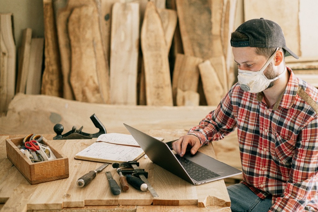 man at wood working bench working on laptop