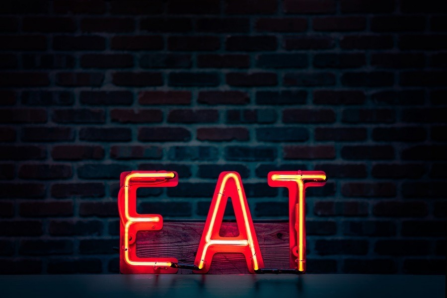 red neon sign against black reading the word eat