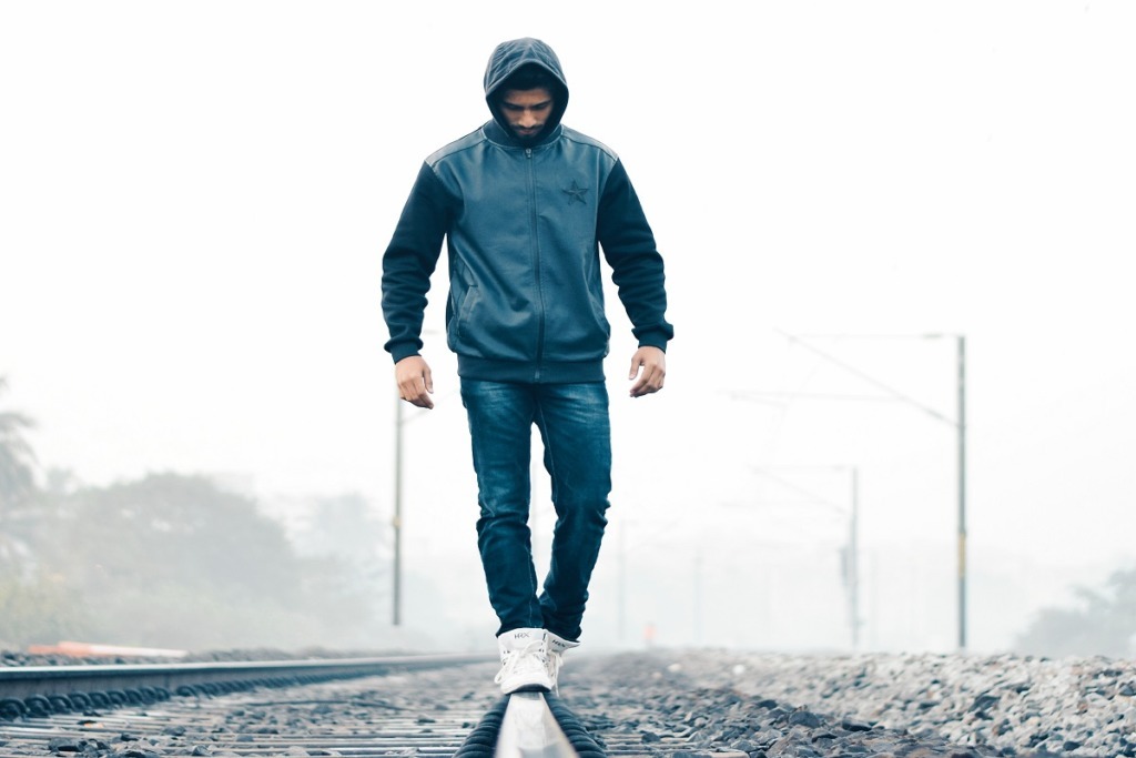 man in blue hoodie walking on train track