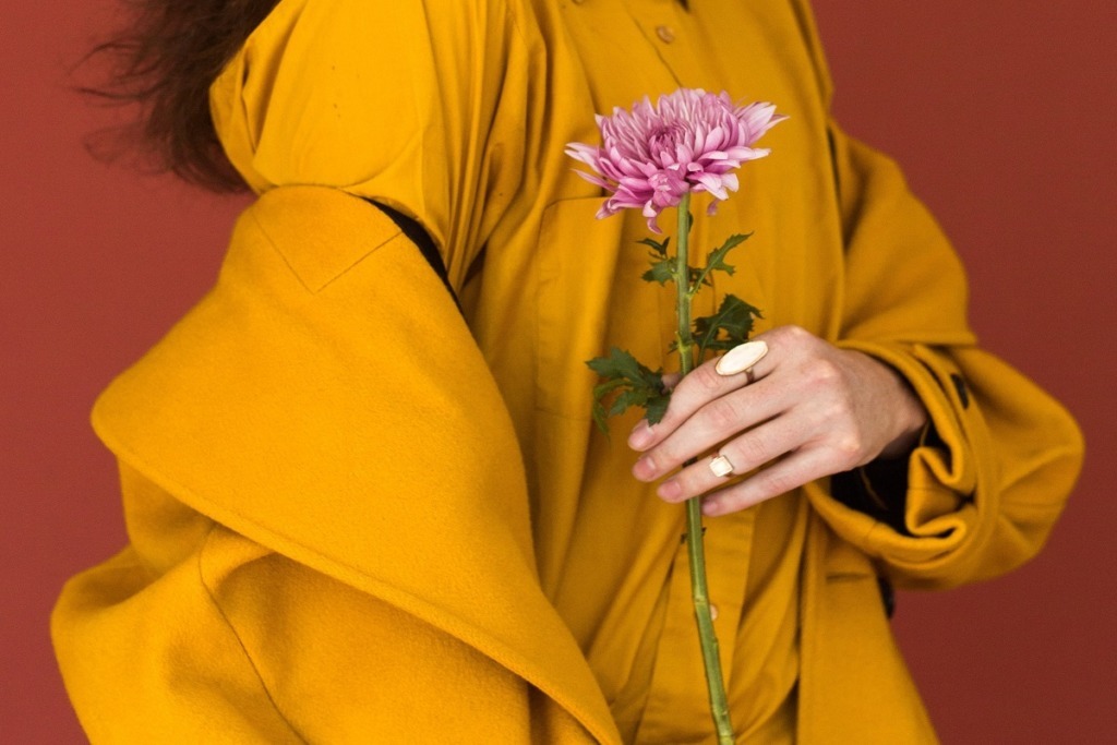 woman in yellow jacket holding pink flower